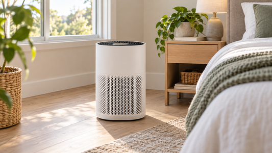 White air purifier beside a nightstand in a sunlit bedroom with a closed window.